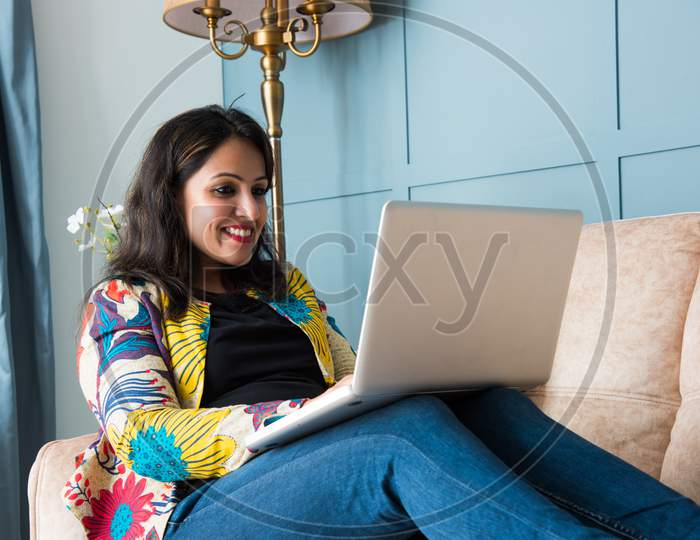 Indian Asian Pretty Woman Using Laptop Computer Or Tablet, Sitting On Sofa
