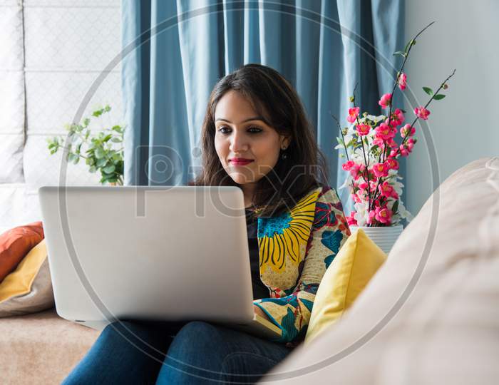 Indian Asian Pretty Woman Using Laptop Computer Or Tablet, Sitting On Sofa
