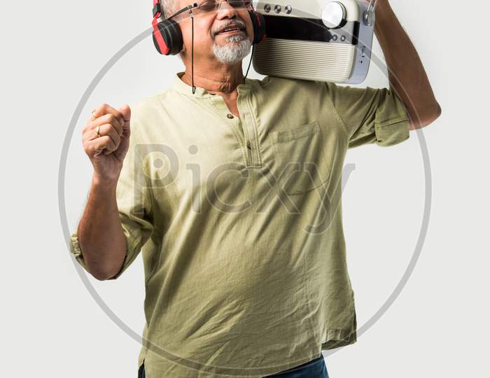 Indian Asian Retired Senior Man Listening Music On Retro Style Radio With Headphones And Dancing