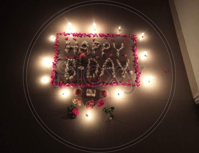 Happy birthday writte in leaf of flowers surrounded by small diyas lighting