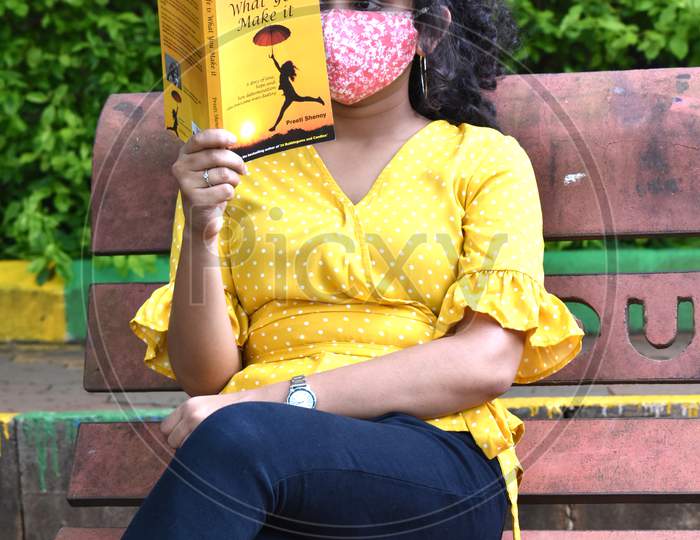 Girl in mask reading book on the bench