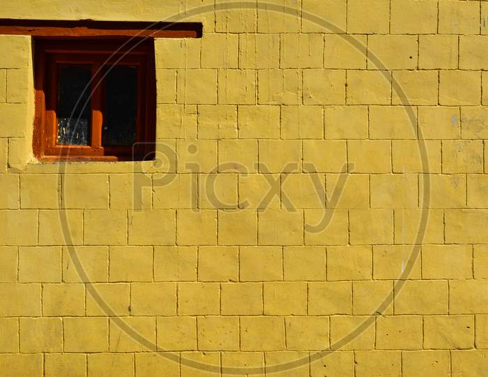 A yellow wall of a house and small orange window