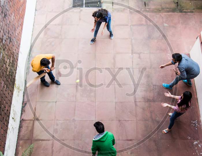 Indian Asian College Students Playing Recreational Fun Cricket Match In Campus Building