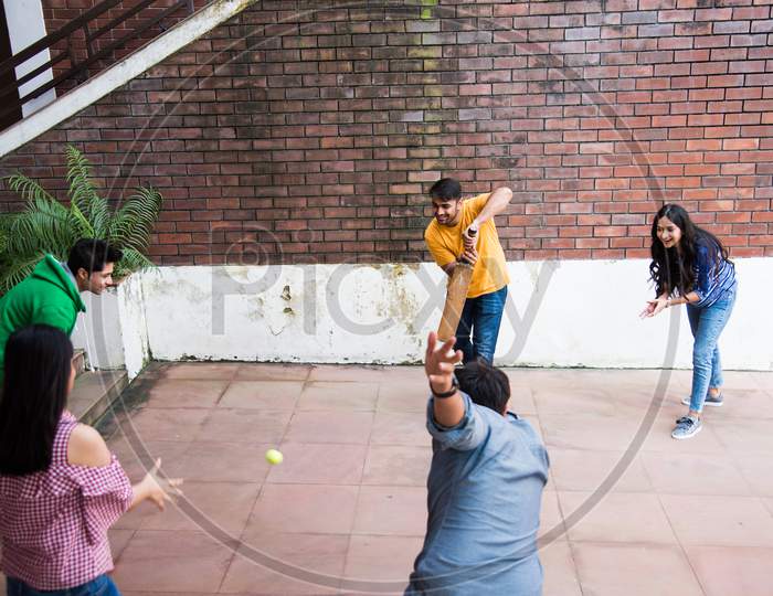 Indian Asian College Students Playing Recreational Fun Cricket Match In Campus Building