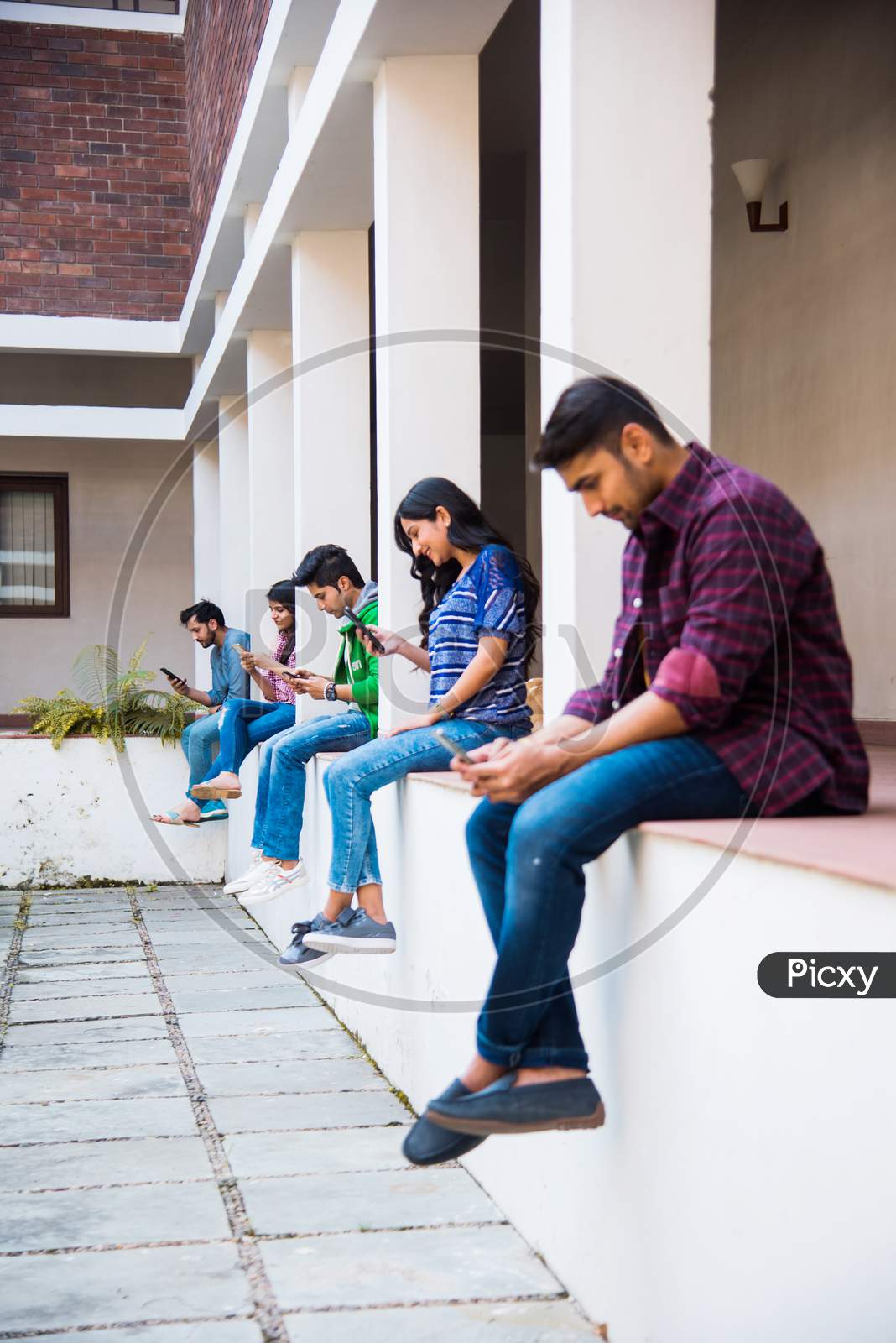 Indian Asian Group Of College Students Using Smartphones For Social Media, Texting, Watching Videos