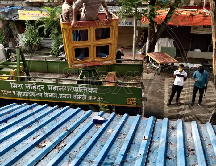 Mumbai, India, October 23, 2020. Professionals at dangerous work, trimming a large tree by use of a telescopic platform truck and wood shredder machine