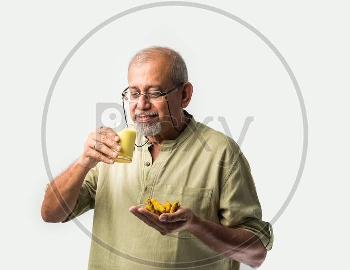 Asian Indian Old Or Retired Man Drinking Turmeric Milk In A Glass