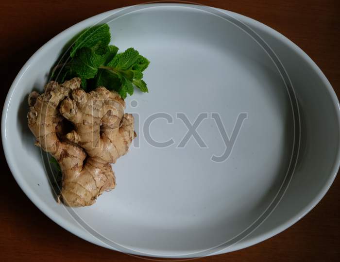 Ginger root and mint leaves in a white tray.