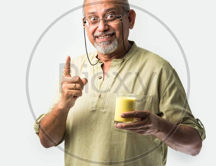 Asian Indian Old Or Retired Man Drinking Turmeric Milk In A Glass