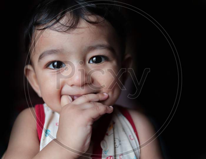 A Head Shot Portrait Of An Adorable Indian Baby Looking At The Camera With Selective Focus On Eyes With Black Background