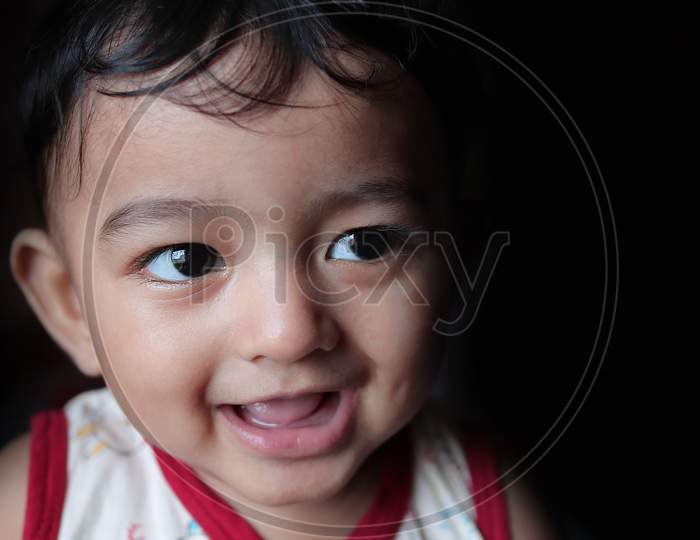 A Head Shot Portrait Of An Adorable Indian Baby Looking At Right With Selective Focus On Front Eye With Copy Space In Black Background