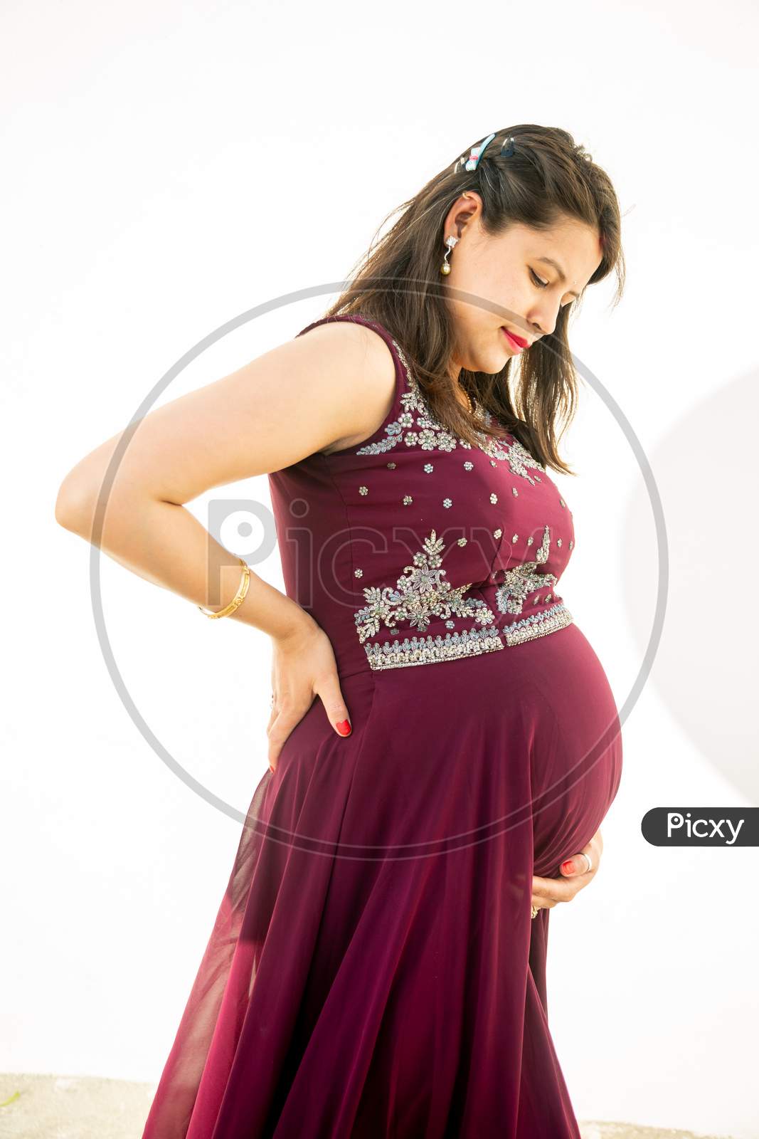 Young Pregnant Woman Looking At Belly Standing Against White Background Outdoor Studio Shot, Happy Female Expecting Baby, Motherhood And Pregnancy Concept