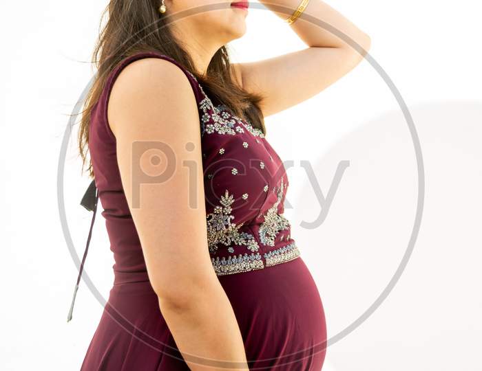 Young Asian Indian Pregnant Woman Looking At Belly Standing Against White Background Outdoor Studio Shot, Happy Female Expecting Baby, Motherhood And Pregnancy Concept.