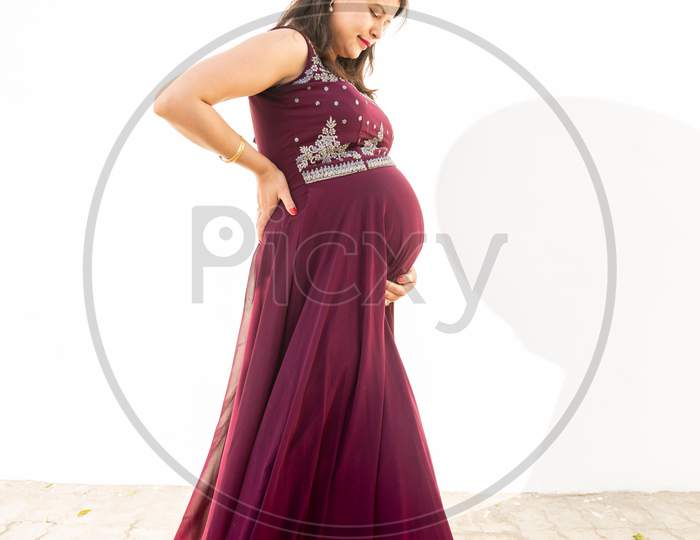Young Pregnant Woman Looking At Belly Standing Against White Background Outdoor Studio Shot, Happy Female Expecting Baby, Motherhood And Pregnancy Concept, Copy Space.