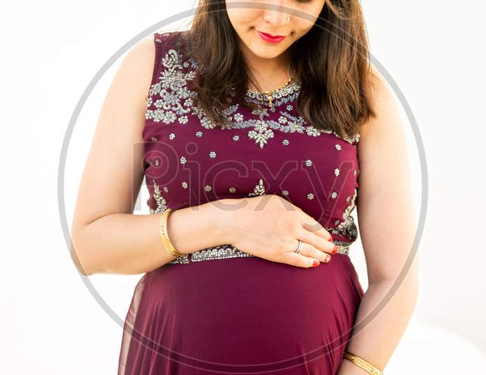 Young Asian Indian Pregnant Woman Looking At Belly Standing Against White Background Outdoor Studio Shot, Happy Female Expecting Baby, Motherhood And Pregnancy Concept, Copy Space.
