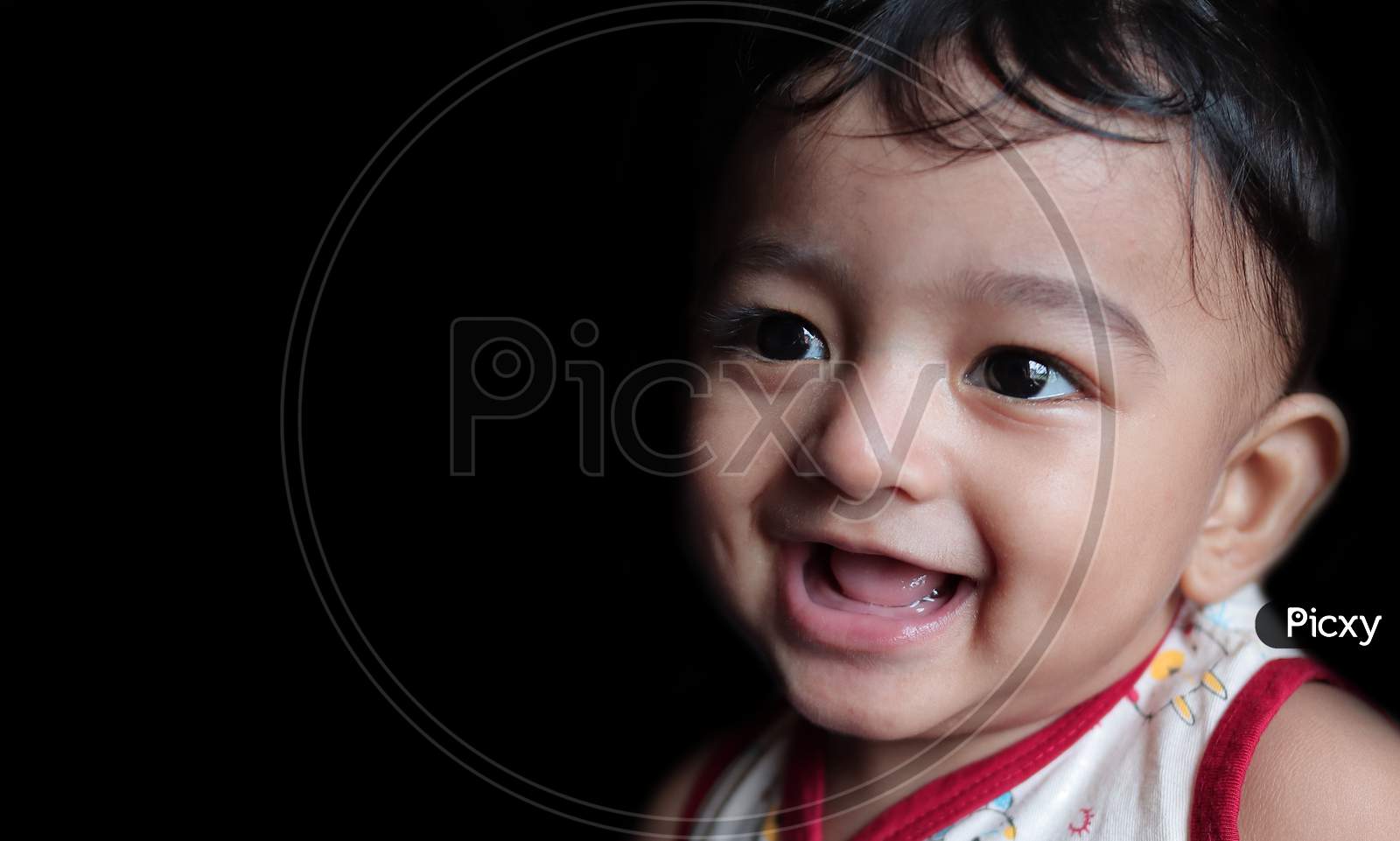 A Head Shot Portrait Of An Adorable Indian Baby Looking At Left With Selective Focus On Front Eye With Copy Space In Black Background