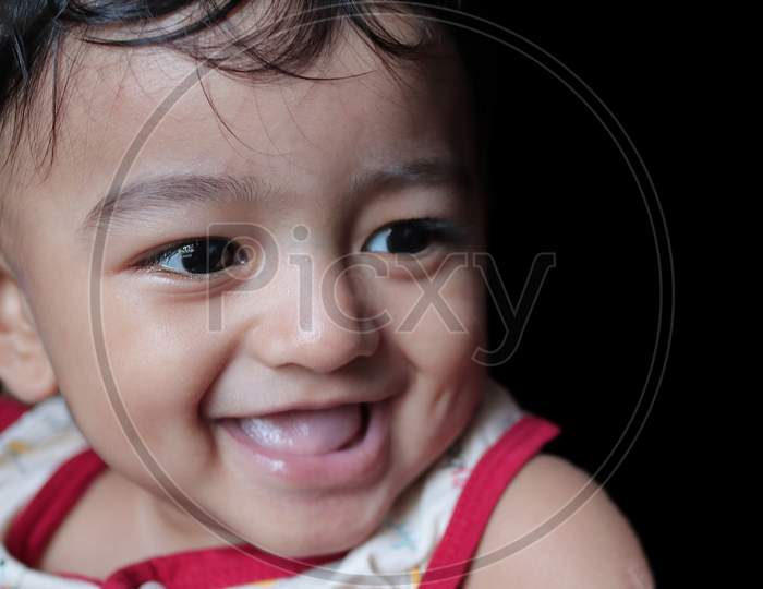 A Portrait Of An Adorable Indian Baby Looking At Downwards And Right With Selective Focus On Front Eye With Copy Space In Black Background