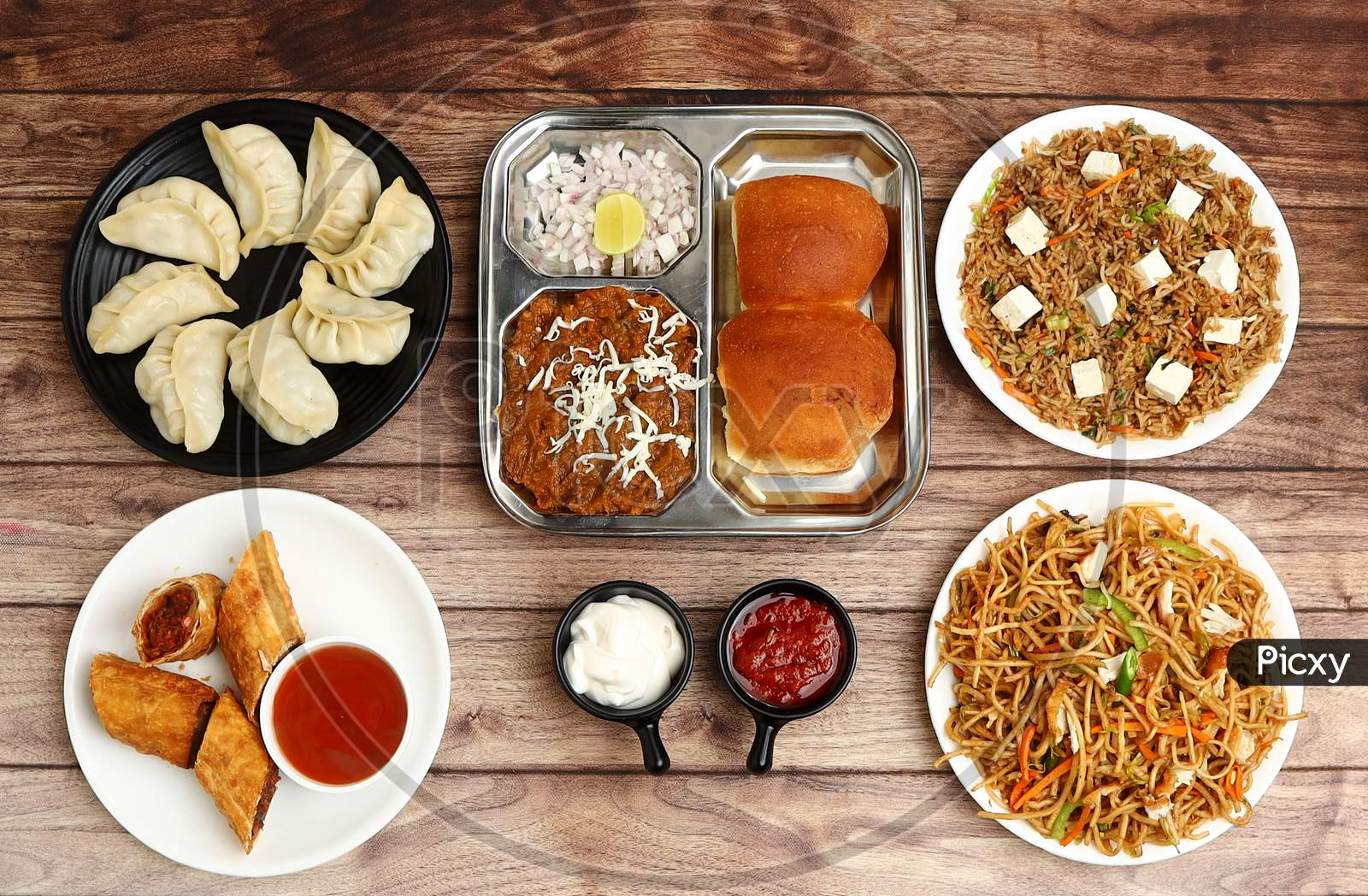 Assorted Indian Food On Wooden Background. Spring Roll,Pav Bhaji, Paneer Fried Rice, Veg Noodles, Momos.. Dishes And Appetizers Of Indian Cuisine
