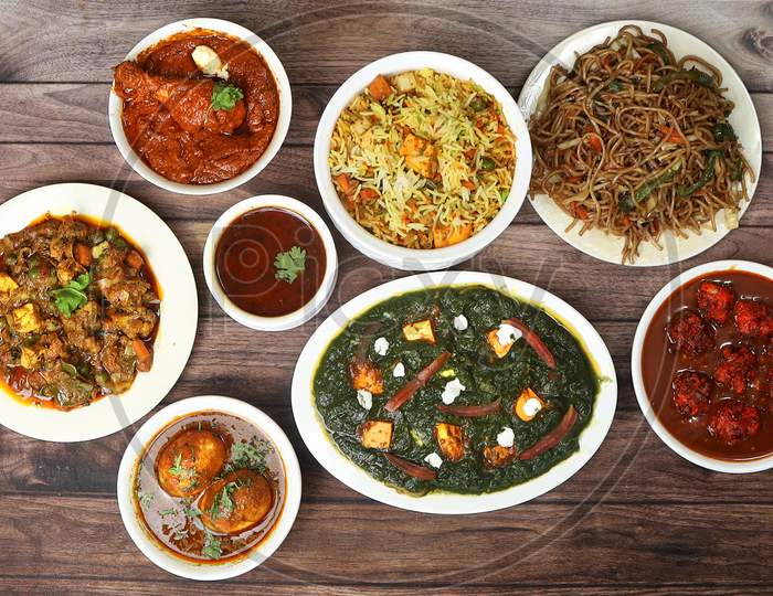 Assorted Indian Food On Wooden Background. Paneer Biryani,Palak Paneer, Butter Chicken Masala,Egg Masala,Noodles,Veg Mix Curry.. Dishes And Appetizers Of Indian Cuisine