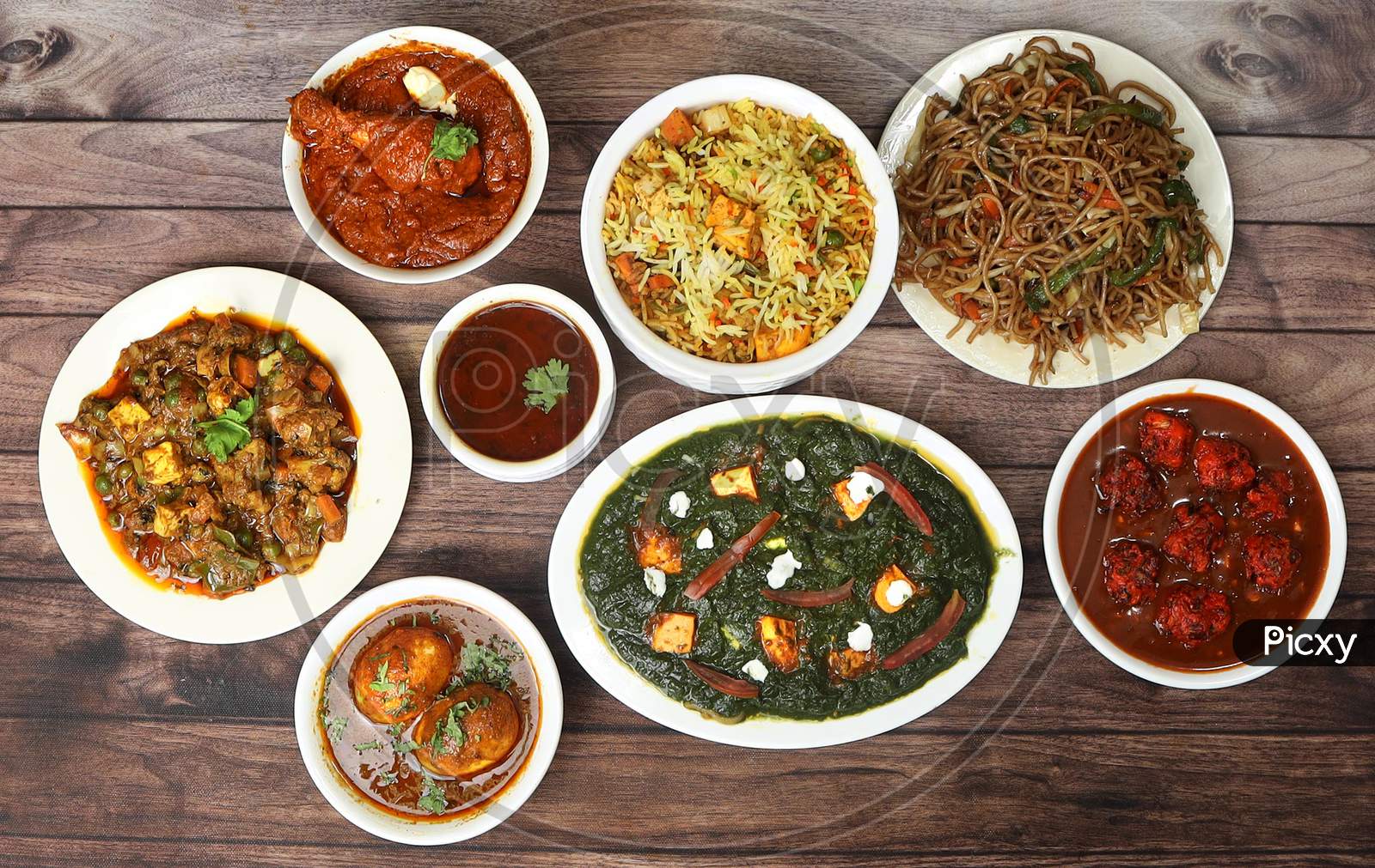 Assorted Indian Food On Wooden Background. Paneer Biryani,Palak Paneer, Butter Chicken Masala,Egg Masala,Noodles,Veg Mix Curry.. Dishes And Appetizers Of Indian Cuisine