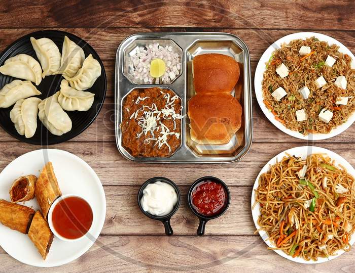 Assorted Indian Food On Wooden Background. Spring Roll,Pav Bhaji, Paneer Fried Rice, Veg Noodles, Momos.. Dishes And Appetizers Of Indian Cuisine