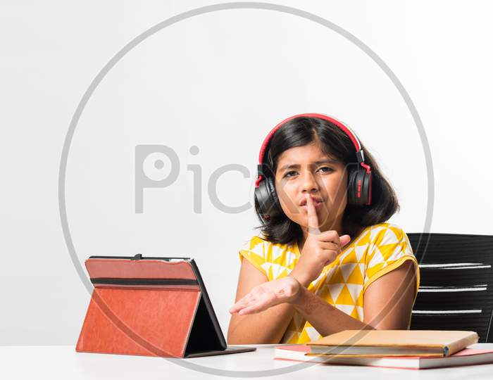 Indian Asian Small School Girl Learning Online Or Attending School Using Tablet Or Laptop Computer