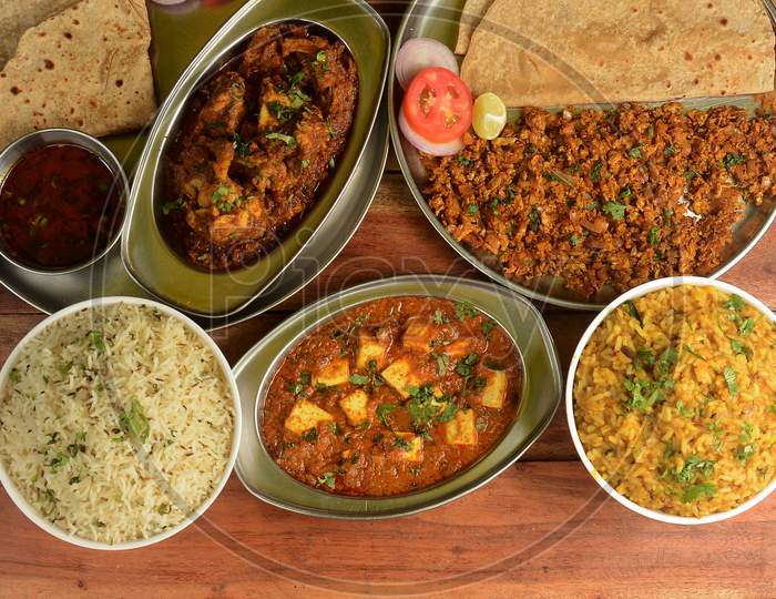 Assorted Indian Food On Wooden Background. Pepper Chicken,Paneer Butter Masala, Jeera Rice & Chapati..Dishes And Appetizers Of Indian Cuisine