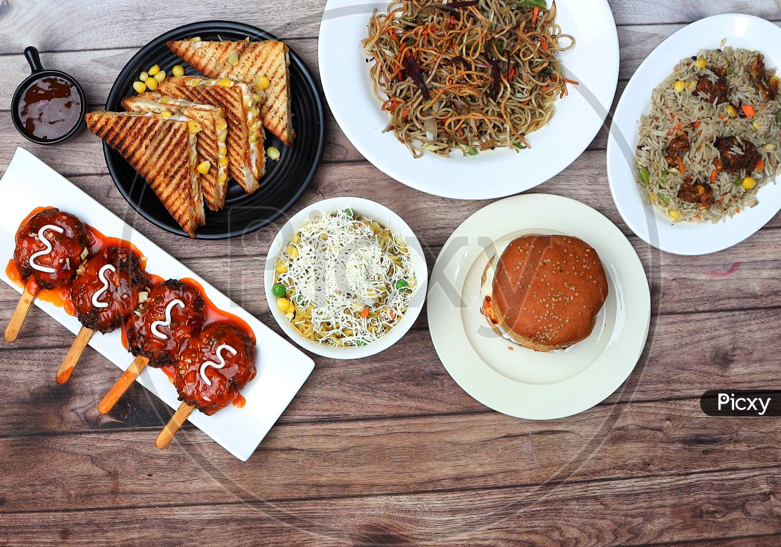 Assorted Indian Food On Wooden Background.Veg Noodles, Manchurian Fried Rice, Cheese Corn Sandwich, Lollipop And Cheese Maggie.. Dishes And Appetizers Of Indian Cuisine