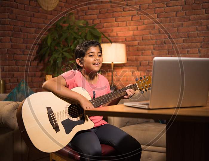 Asian Indian Cute Little Girl Learning Music At Home Attending Online Class On Laptop Or Tablet Pc