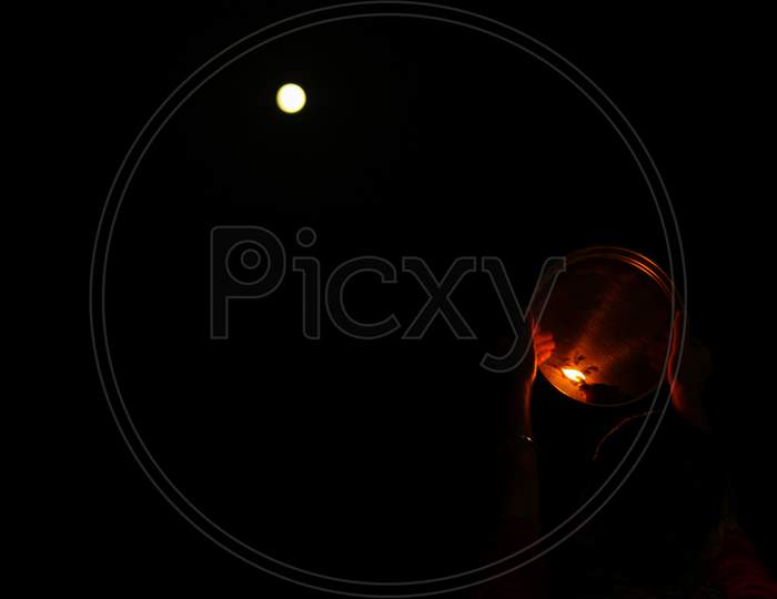 night view of karwa Chauth pooja with a glowing diya against the moon