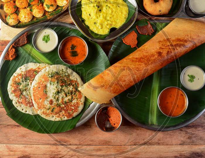 Assorted South Indian Breakfast Foods On Wooden Background. Ghee Dosa, Uttappam,Medhu Vada,Pongal,Podi Idly And Chutney.. Dishes And Appetizers Of Indian Cuisine