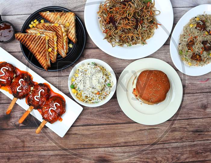 Assorted Indian Food On Wooden Background.Veg Noodles, Manchurian Fried Rice, Cheese Corn Sandwich, Lollipop And Cheese Maggie.. Dishes And Appetizers Of Indian Cuisine