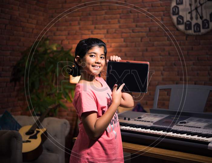 Asian Indian Cute Little Girl Learning Music At Home Attending Online Class On Laptop Or Tablet Pc