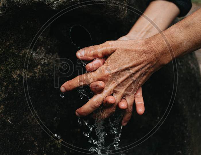 Close Up Of And Old Woman Washing Her Hands In A Rural Font With The Water Frozen