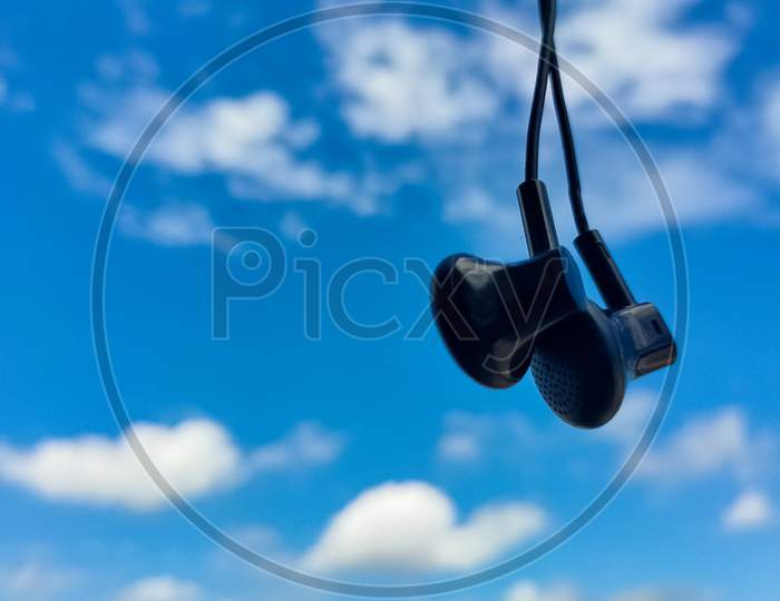Hanging earphones with blurred blue cloudy sky.