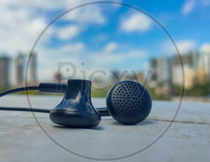 Picture of earphones with blurred background of buildings and Blue cloudy sky.
