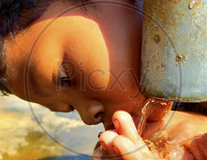 A boy drinking water hold with hands to tubewell.