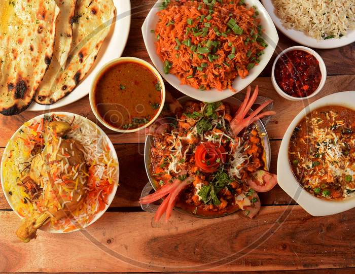 Assorted indian foods chicken biryani,butter naan,schezwan fried rice,mutter paneer and jeera rice on wooden background. Dishes and appetizers of indian cuisine