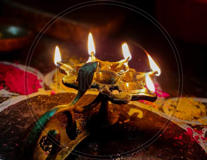 A Glowing Multi Flame Lamp Commonly Known As Panchapradip. A Holy Thing Used As An Offering To God For Worship. Surrounded By Colourful Rangoli.