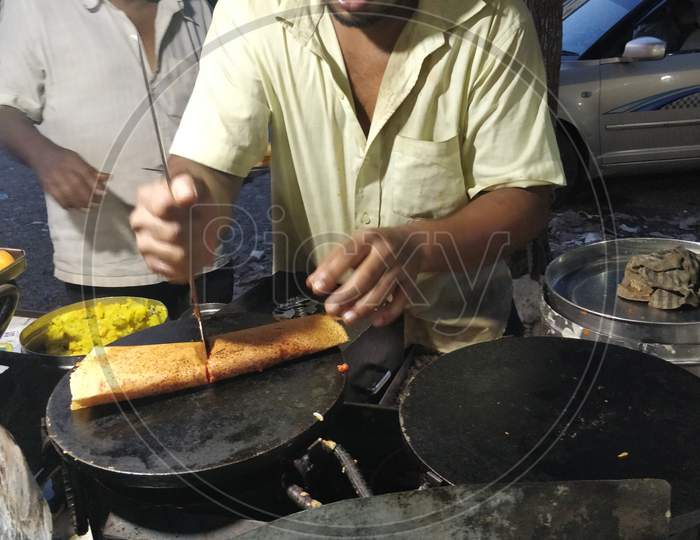 Chef making roadside masala dosa or dosai on a frying pan on market street
