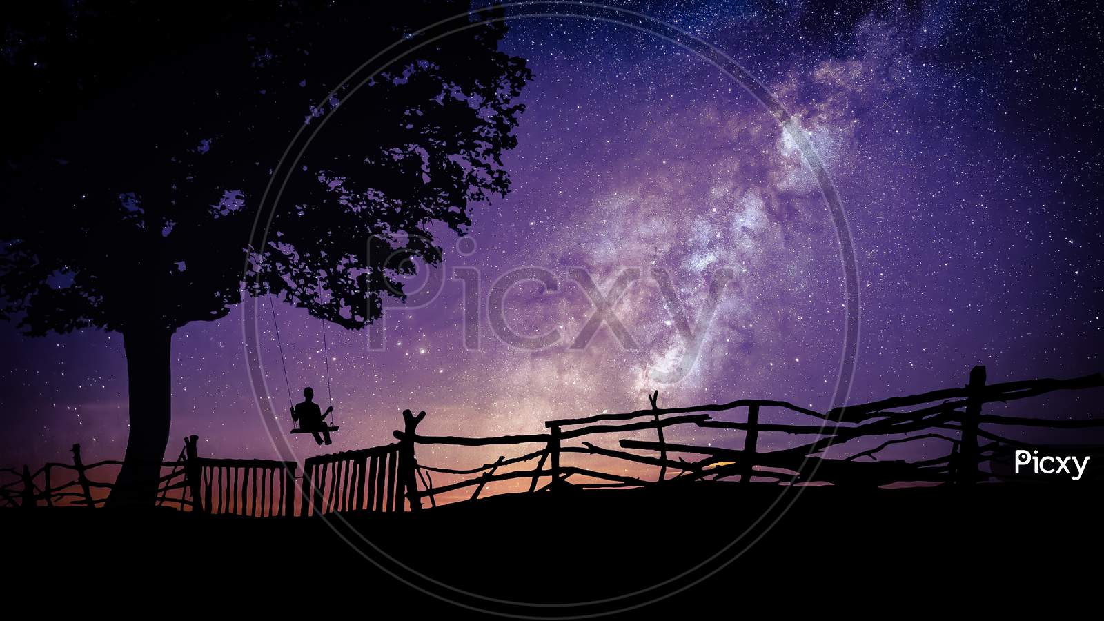 Starry Milky Way sky silhouette with a swinging boy in the tree at night.