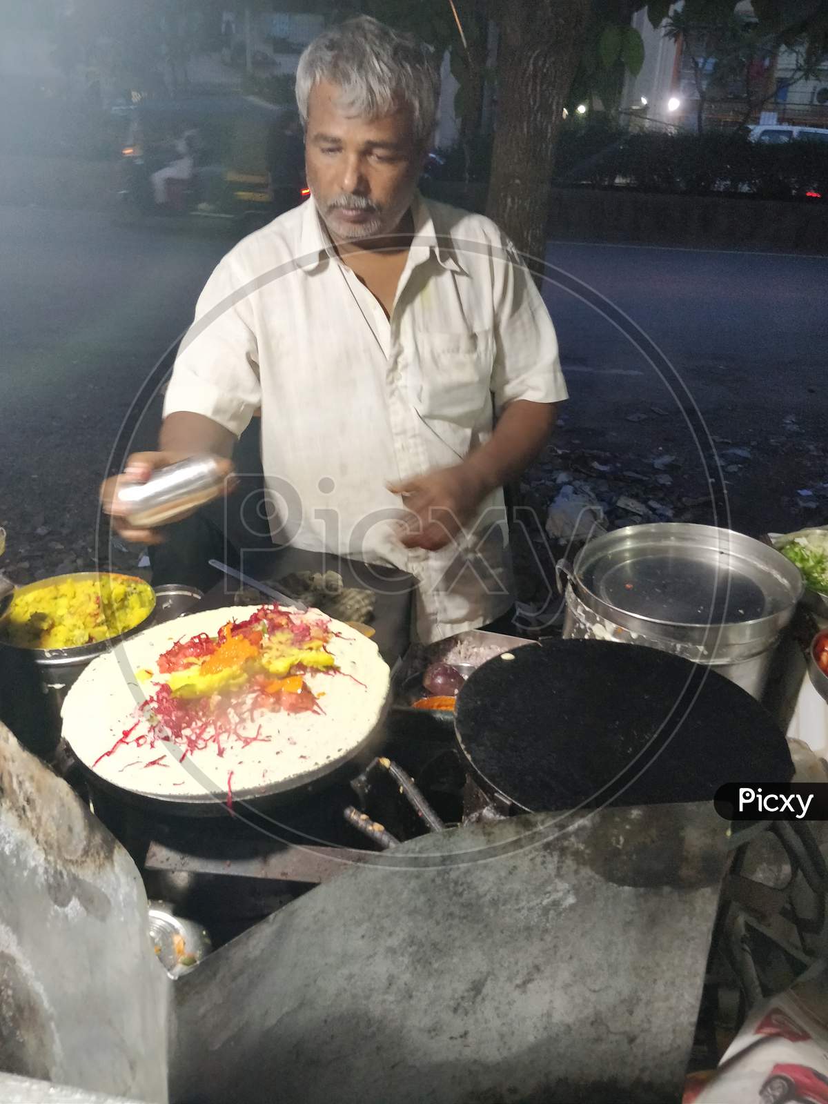 Chef making roadside masala dosa or dosai on a frying pan on market street