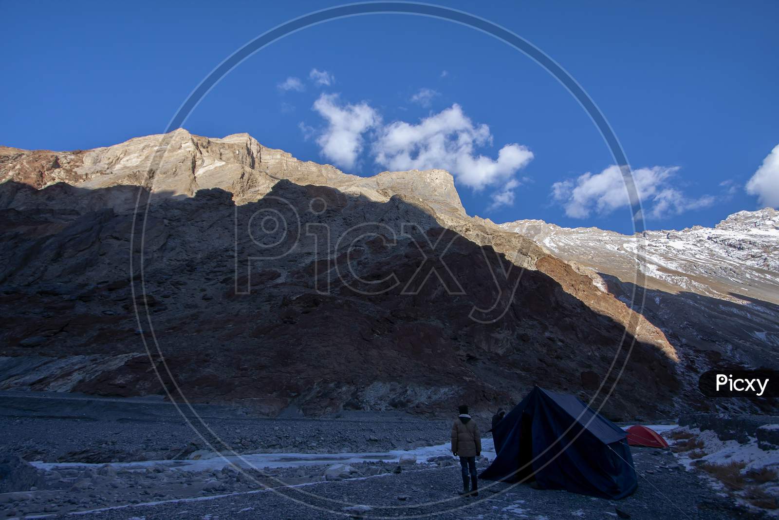 Tenting Ground With Tents In Front Of High Altitude Peaks And Its Shadow In A Cold Sunny Day In The Himalaya In Ladakh