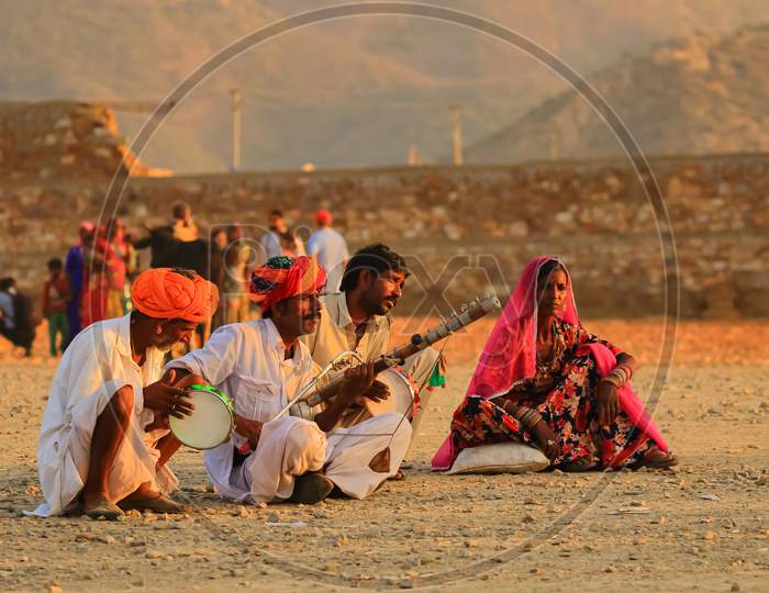 A group of people siting on groA group of people siting on ground and playing tradional Indian musical instrumentsund and playing tradional Indian musical instruments
