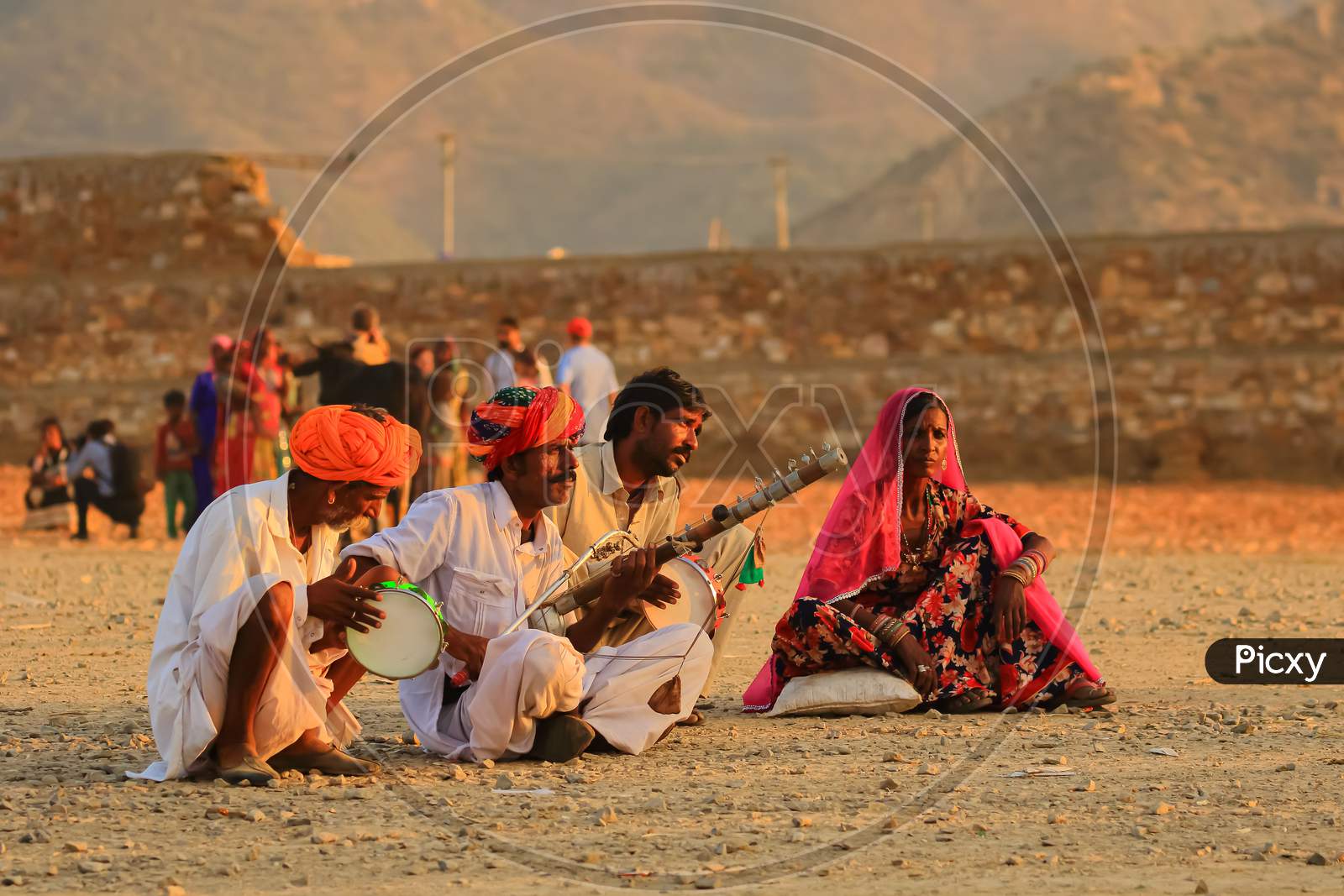 A group of people siting on groA group of people siting on ground and playing tradional Indian musical instrumentsund and playing tradional Indian musical instruments