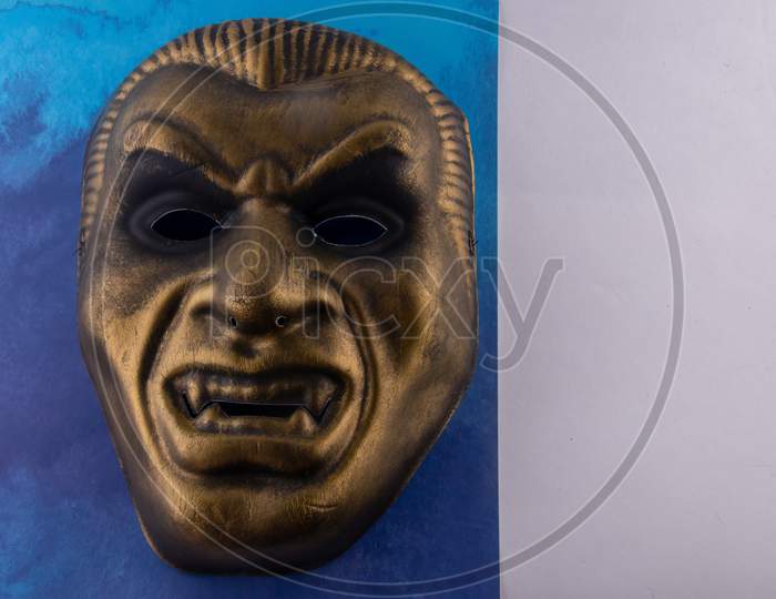 Gold Vampire Mask Close Up On Blue Backgound. Concept Of Halloween Fun For Kids