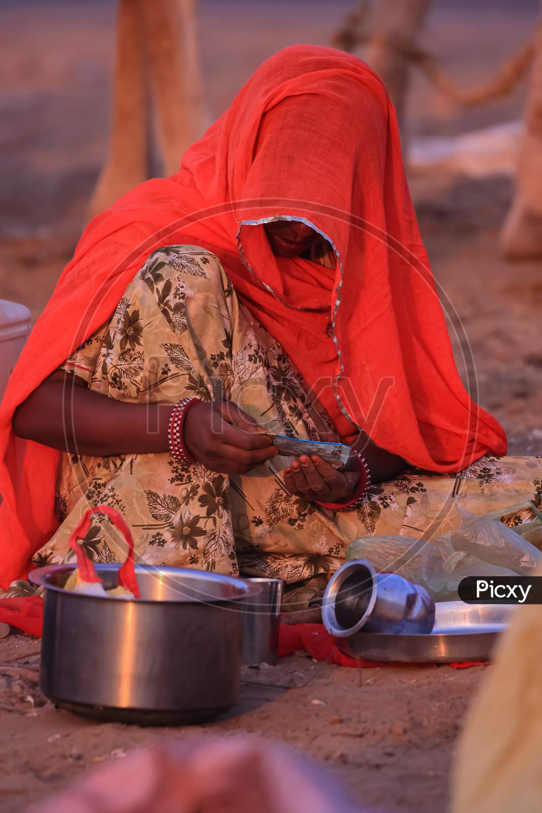 A women wearing an orange traditional Rajasthani dress covering her face and siting on ground