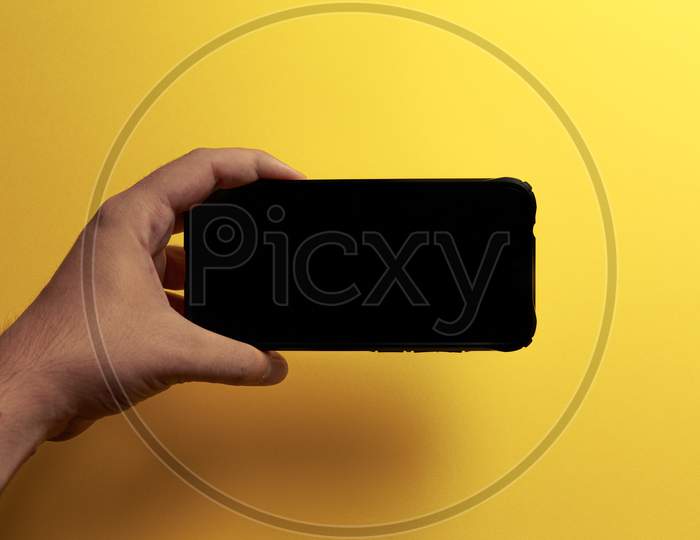 Young Hand Showing Something On A Phone Screen With Copy Space Over A Yellow Background In Horizontal