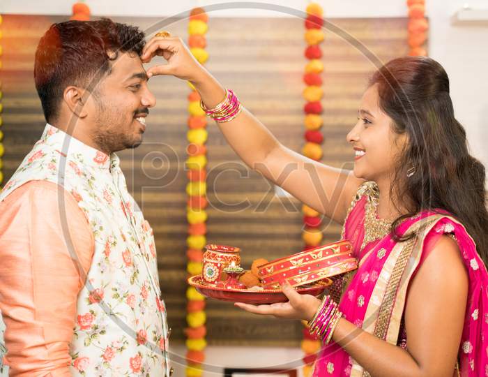 Woman Applying Thilaka Or Mark To His Partner Or Husband'S Forehead During Karwa Chauth Festival Celebration While Both In Traditional Dress.