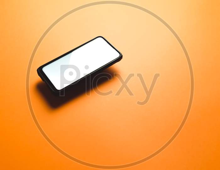 Minimalistic Mock Up Flat Image Design With A Floating Mobile Phone With Copy Space And White Scree To Write Over It Over A Flat Orange Background